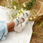 Person wearing socks with butterfly design in a natural setting with flowers and a basket nearby.