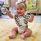 A baby sitting on the floor wearing a giraffe print bib with off-white giraffe applique and a plush terry cloth back.
