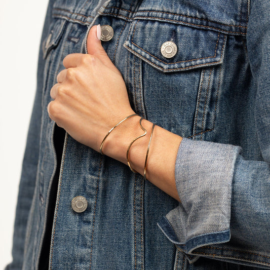 Arm of woman wearing denim jacket with an Emily Brass Bangle and two Hammered Brass Bangles, modern and minimalist.