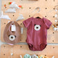Baby onesie and bib with bear design hanging on a wooden pegboard with toys.