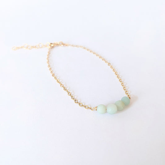 Woman in beige shirt wearing 14k gold fillled bracelet with four amazonite beads.