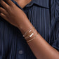 Woman in a navy pleated shirt wearing a mixed metals bracelet stack with a brass bangle, sterling silver and 14k gold filled paperclip and freshwater pearl bracelets.