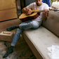 Man playing an acoustic guitar on a couch wearing dark gray crew socks with music notes