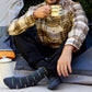Person sitting outdoors, wearing plaid shirt and dark gray fish-patterned crew socks, holding a mug.