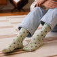 Person wearing light green crew socks with floral design sitting on a striped rug.