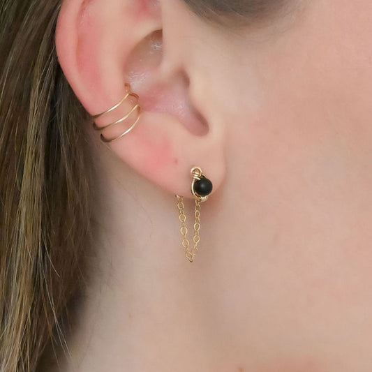 a pair of gold stud earrings on a display rack with dainty chain earring jackets attached to form loops.