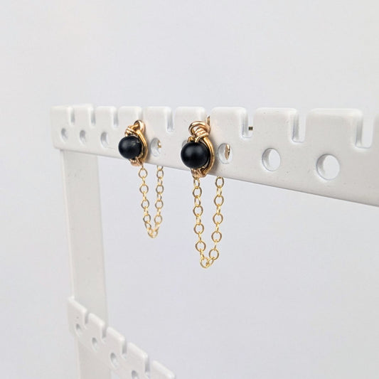 a pair of gold stud earrings on a display rack with dainty chain earring jackets attached to form loops.