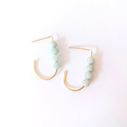 Close-up of a woman wearing a J hoop aarring with four small round amazonite gemstones.