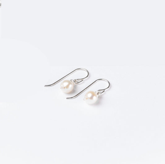 A woman wearing Leeda Freshwater Pearl Earrings in Sterling Silver, featuring a single pearl drop and hammered detailing.