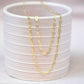 a gold paperclip chain necklace and bracelet draped over the edge of a pink ceramic cup on a pink backdrop