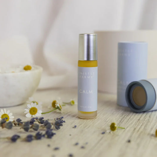 Thistle Farms Calm essential oil roll-on bottle and packaging on a light blue background