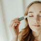 Woman applying Thistle Farms essential oil roll-on blend to her forehead.