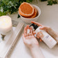 Person putting Thistle Farms Grapefruit Jasmine hand lotion into their hand. Background of grapefruit in a bowl.
