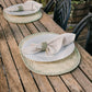 Plates with napkins on woven placemats on a wooden table outdoors.