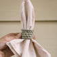 Napkin held by a hand with a green crocheted napkin ring against a beige background