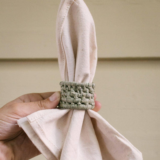 Napkin held by a hand with a green crocheted napkin ring against a beige background