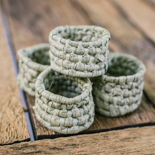 Napkin held by a hand with a green crocheted napkin ring against a beige background