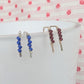 Two pairs of beaded earrings on a white surface with a pink polka dot background