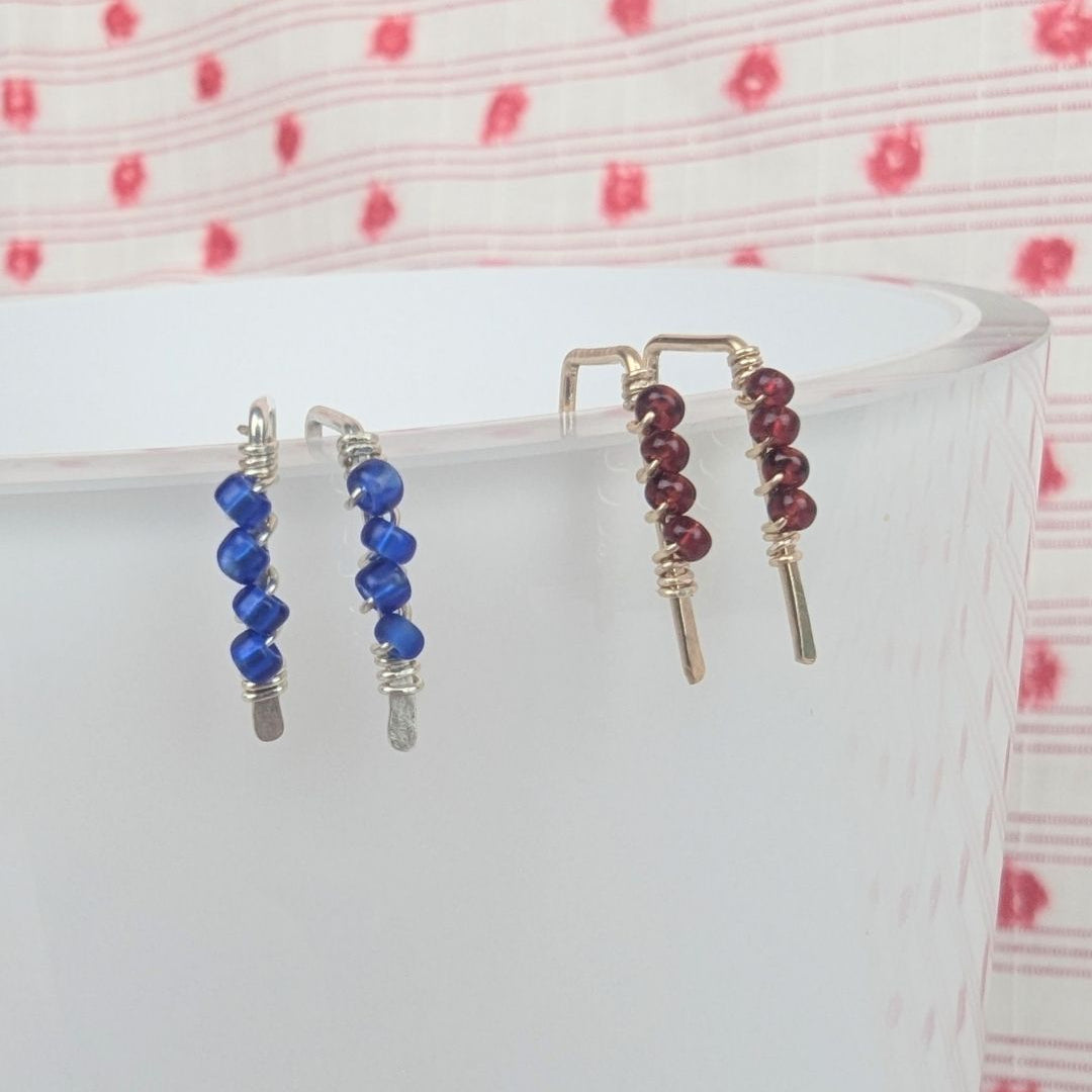Two pairs of beaded earrings on a white surface with a pink polka dot background