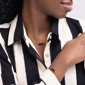 Woman in a black and white striped shirt wearing Jordan Black Onyx Necklace, Bracelet, and J Hoop Earrings in 14k gold filled.