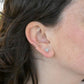 Close-up of an ear wearing sterling silver stud earrings with a light green bead and a sterling silver ear cuff