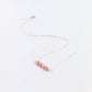 silver necklace with four pink beads at the center on a white background