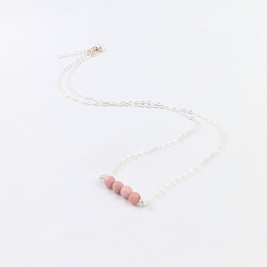 silver necklace with four pink beads at the center on a white background