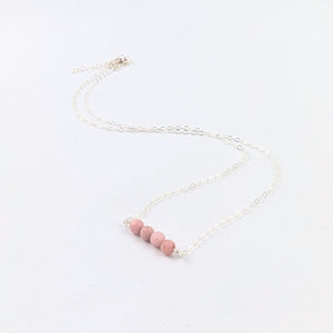 silver necklace with four pink beads at the center on a white background