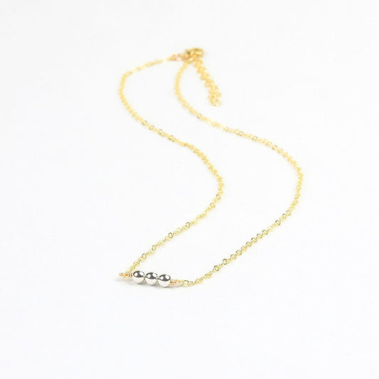 Gold necklace with three silver beads on a white background