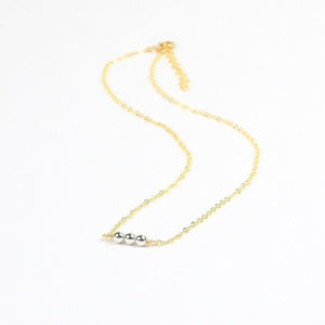 Gold necklace with three silver beads on a white background