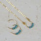 a pair of small gold hoop earrings with turquoise beads and a matching necklace on a stone background