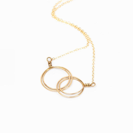 The Zomi Circles of Unity Necklace in 14k gold filled features interlocking circles and is modeled by a young woman in a brown sweater.