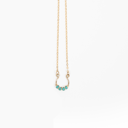 A close-up of a woman wearing a beige shirt and the Moab Western Beaded Necklace in 14k gold filled. Horseshoe design with turquoise beads.