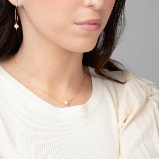 A woman in a white sweater wearing the Leeda Pearl Necklace, a dainty 14k gold filled necklace with a single freshwater pearl.