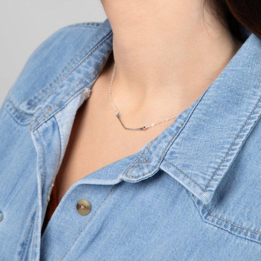 A woman in a blue denim shirt showcasing a sterling silver chevron pendant necklace.