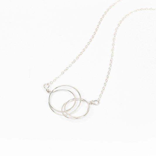 The Zomi Circles of Unity Necklace, a sterling silver necklace featuring interlocking circles, worn by a person in a black sweater.