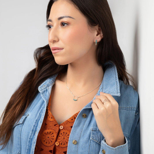 A woman wearing a denim jacket and an orange top with geometric patterns, showcasing the Moab Western Beaded Necklace in sterling silver necklace with turquoise beads.