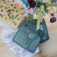Green patterned potholders on a white cloth with a pizza and flowers on a wooden surface