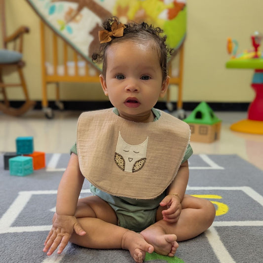 tan baby bib with owl design on a white background