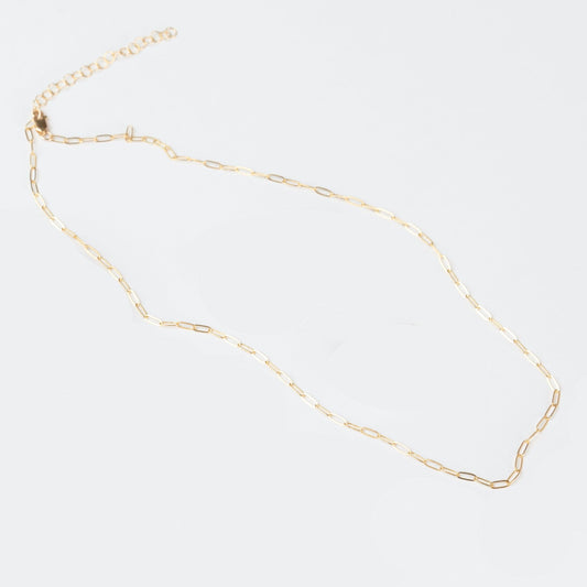 A woman wearing a light brown blouse showcasing a delicate minimalist paperclip chain necklace in 14k gold filled.