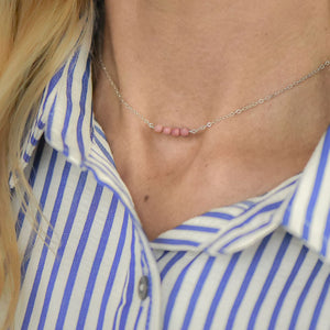 close up of the neck of a blonde woman wearing a silver chain necklace with four pink rhodonite beads at the center