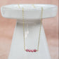 gold chain necklace adorned with four pink rhodonite beads at the center hanging from a white pedastal on a pink background