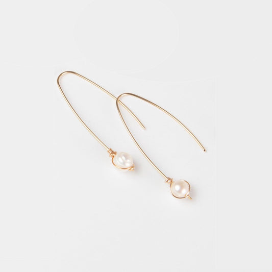 A young woman wearing Rana Pearl Threader Earrings in 14k gold filled, which are hanging from the ear and have a small freshwater pearl detail.