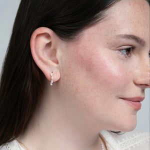 A woman wearing a pair of 14k gold filled C hoop earrings with rice pearls.