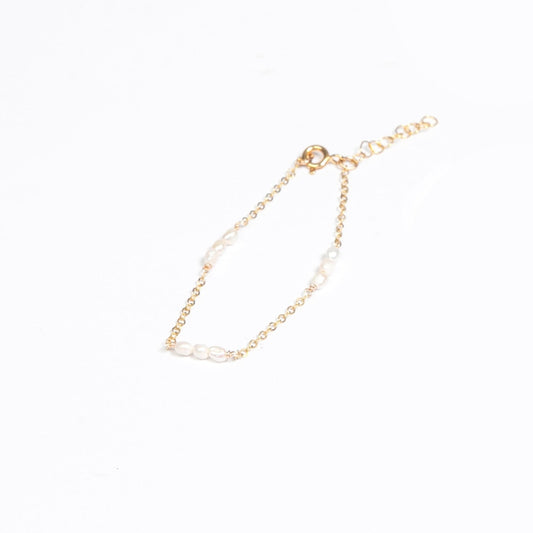 A woman in a white lace shirt is showcasing a 14k gold filled bracelet with rice pearl stations on her wrist.