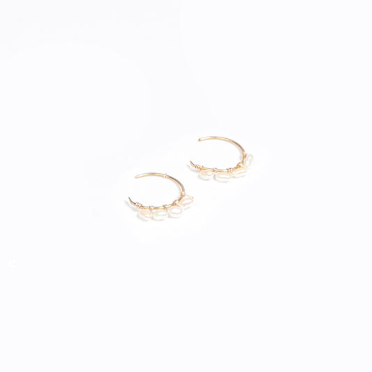 A woman wearing a pair of 14k gold filled C hoop earrings with rice pearls.
