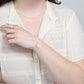 A woman in a white lace shirt is showcasing a 14k gold filled bracelet with rice pearl stations on her wrist.