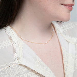 A woman in a white lace top showcasing a 14k gold filled necklace with freshwater rice pearl stations.