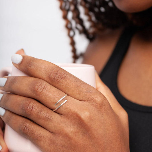 A woman holding a white mug, wearing a simple sterling silver wrap ring on one of their fingers.