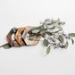 set of hand carved napkin rings holding a stem of eucalyptus on a white background